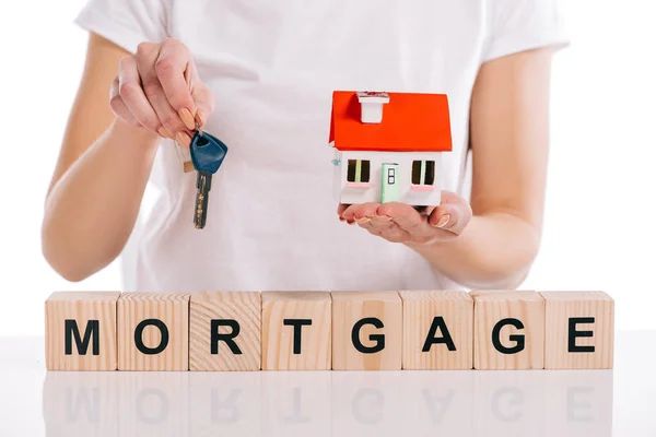 Partial view of woman holding house model and keys near wooden cubes with mortgage lettering isolated on white — Stock Photo