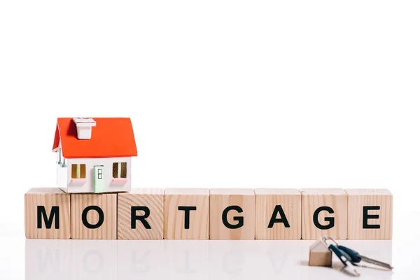 Bloques de madera con letras hipotecarias, modelo de casa y llaves aisladas en blanco - foto de stock