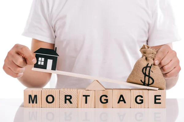 Partial view of man holding moneybag and paper house on scales on cubes with mortgage lettering isolated on white — Stock Photo