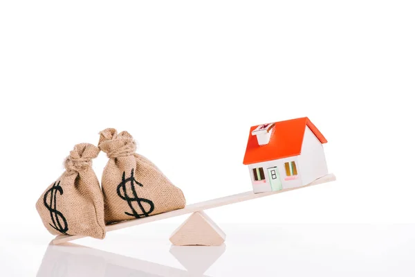 Básculas con bolsas de dinero y modelo de casa aislado en blanco, concepto de hipoteca - foto de stock