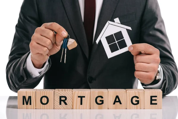 Cropped view of mortgage broker holding paper house and keys near wooden blocks isolated on white — Stock Photo