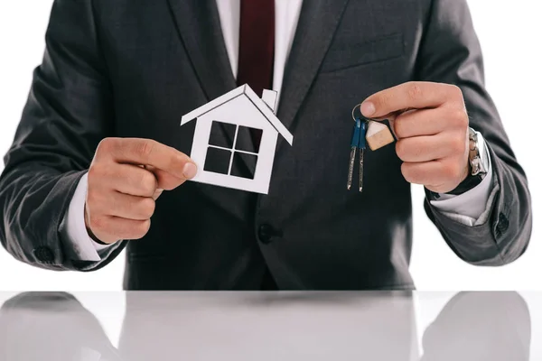 Vue recadrée du courtier hypothécaire tenant maison de papier et clés isolées sur blanc — Photo de stock