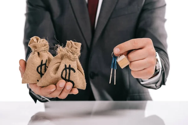 Vue recadrée du courtier hypothécaire détenant des clés et des sacs d'argent isolés sur blanc — Photo de stock