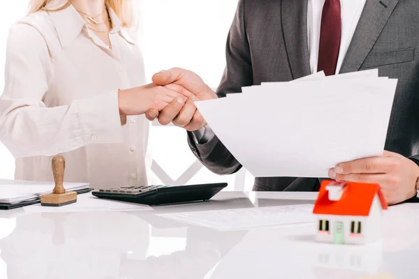 Cropped view of businessman and businesswoman shaking hands and holding papers isolated on white, mortgage concept — Stock Photo