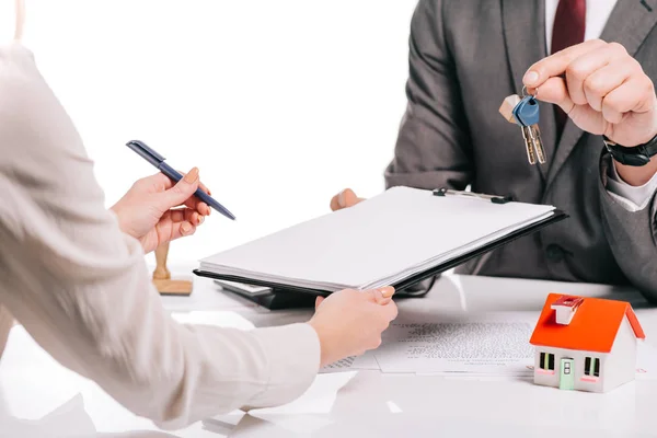 Vista recortada del corredor de hipotecas y la mujer haciendo trato y la celebración de llaves aisladas en blanco, concepto de hipoteca - foto de stock