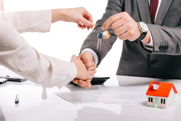 Cropped view of mortgage broker shaking hands with woman and holding keys isolated on white, mortgage concept — Stock Photo