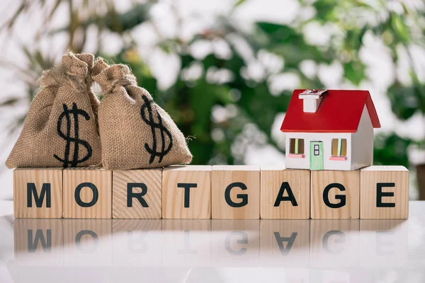 Selective focus of moneybags with dollar signs and house model on wooden cubes with letters, mortgage concept — Stock Photo