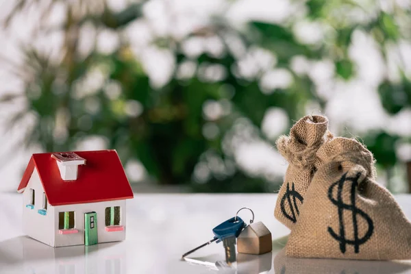 Selective focus of keys, house model and moneybags with dollar signs on white desk, mortgage concept — Stock Photo