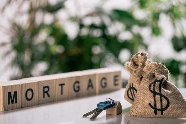 Selective focus of keys, wooden cubes and moneybags with dollar signs on white desk, mortgage concept — Stock Photo