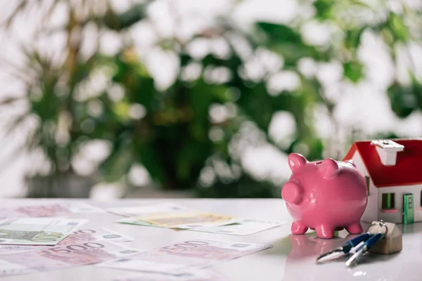 Foco seletivo das notas de euro, chaves, banco piggy e modelo de casa na mesa branca, conceito de hipoteca — Fotografia de Stock