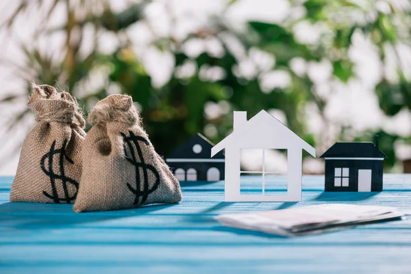 Enfoque selectivo de casas de papel y bolsas de dinero con signos de dólar en el escritorio de madera, concepto de hipoteca - foto de stock