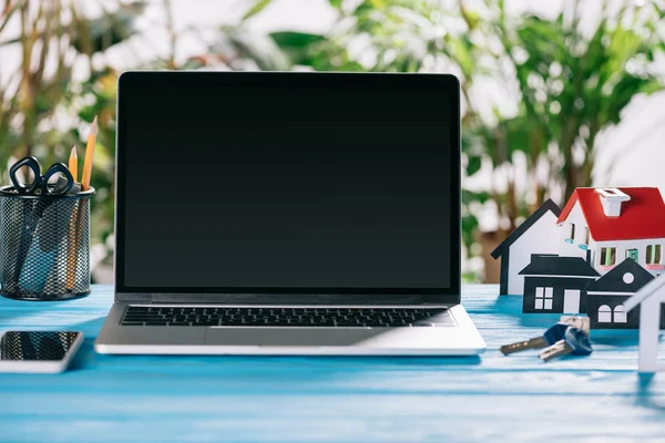 Selektiver Fokus von Smartphone, Laptop mit leerem Bildschirm und Tasten in der Nähe von Papierhäusern auf Holzschreibtisch, Hypothekenkonzept — Stockfoto