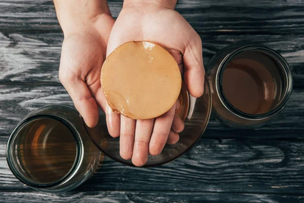 Top view of bottled tea and kombucha mushroom in hands — Stock Photo