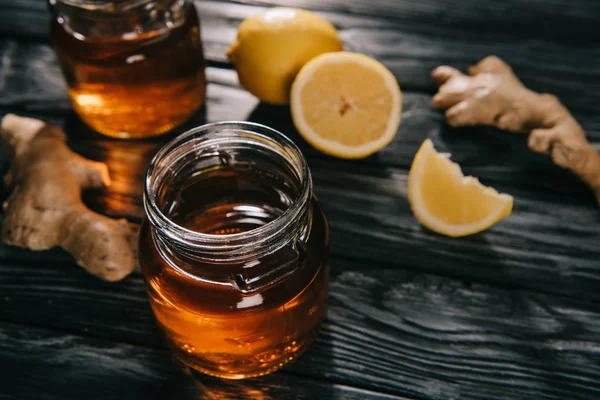 Селективный фокус чая в стеклянной банке на деревянном столе с корнями имбиря и лимонами — стоковое фото
