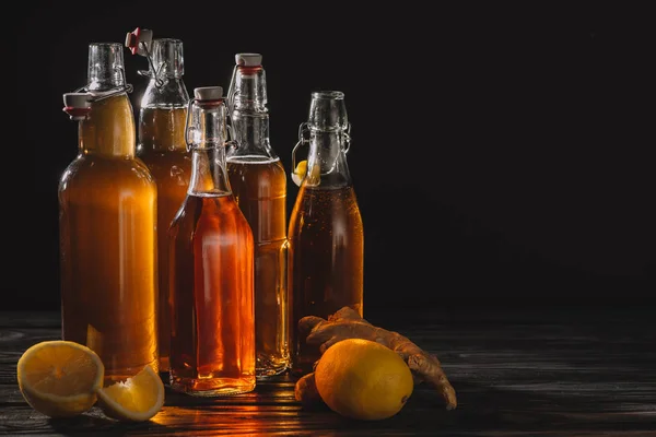 Té orgánico casero en botellas de vidrio con limones y raíz de jengibre aislado en negro - foto de stock