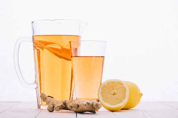 Чай с лимоном и корень имбиря в стекле и банка на деревянном столе изолированы на белом — стоковое фото