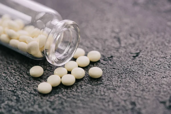 Selective focus of scattered white pills from bottle on grey surface — Stock Photo