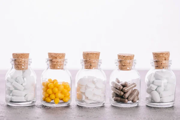 Linha de garrafas com rolhas e comprimidos diferentes isolados em branco — Fotografia de Stock