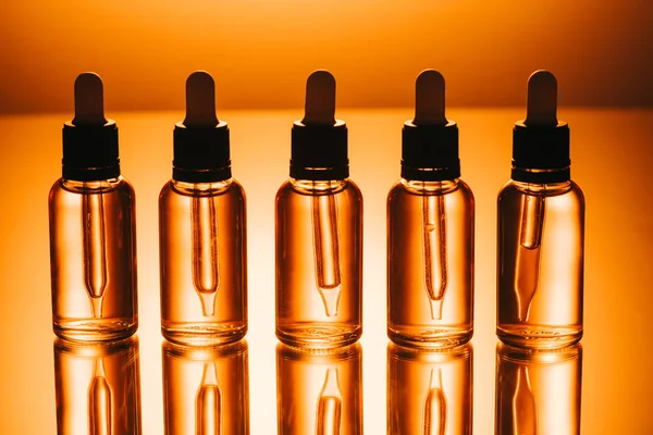 Fila de aceite de cbd en botellas con goteros sobre fondo naranja - foto de stock