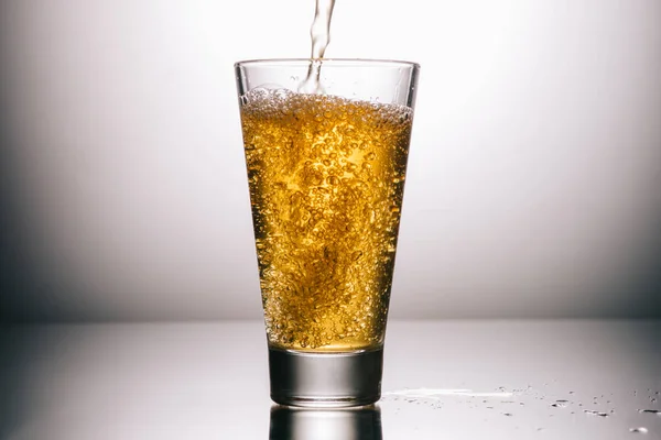 Plein verre de thé et éclaboussures sur fond gris — Photo de stock