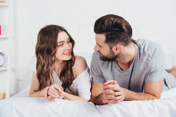 Young loving couple lying on soft white bedding — Stock Photo