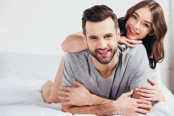 Selective focus of young happy couple lying on soft white bedding — Stock Photo