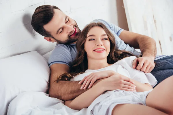 Joven adulto amante pareja sonriendo y gentil abrazo en la cama - foto de stock