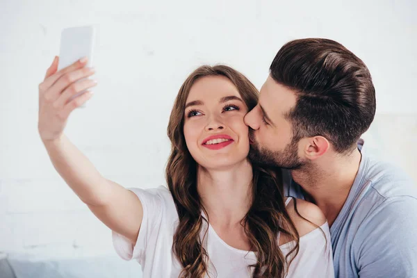 Novio besar novia mientras toma selfie en dormitorio - foto de stock