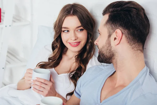 Couple adulte relaxant et tenant des tasses tandis que la femme regardant dans les yeux de l'homme — Photo de stock