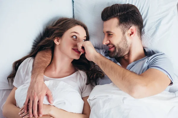 Молодой любящий мужчина нежно обнимает женщину в постели и трогает нос — стоковое фото