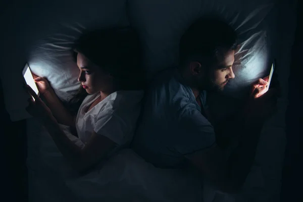 Couple couché dos à dos au lit et utilisant des smartphones la nuit — Photo de stock