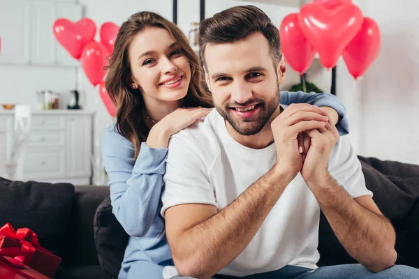 Feliz jovem casal celebrando dia dos namorados no quarto com balões em forma de coração — Fotografia de Stock
