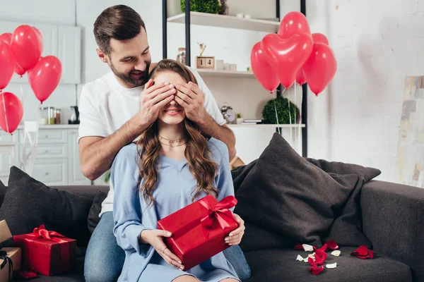 Uomo amorevole che copre gli occhi della donna con le mani in camera con palloncini a forma di cuore — Foto stock