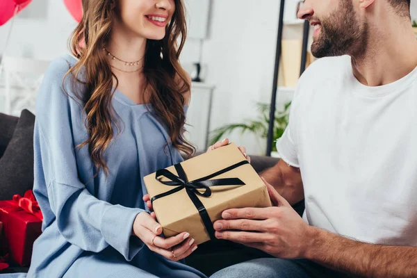 Vista recortada de la joven pareja feliz sosteniendo caja de regalo con cinta — Stock Photo