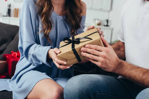 Vista parcial de la joven pareja feliz sosteniendo caja de regalo con cinta - foto de stock