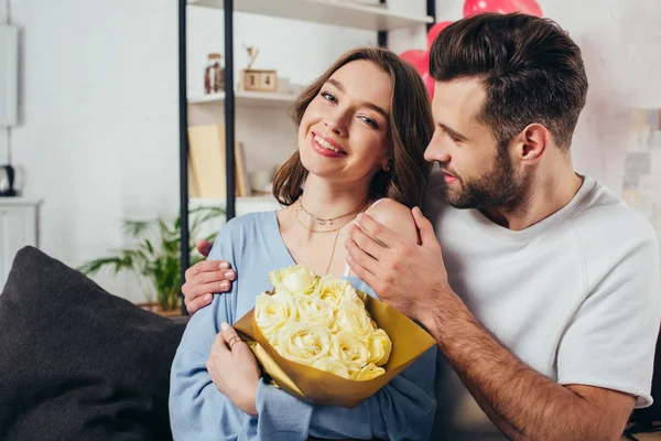 Alegre pareja celebrando día de San Valentín mientras joven abrazando novia con ramo de rosas - foto de stock