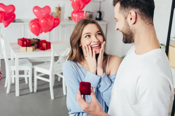 Selective focus of surprised girl touching face while man doing proposal at valentines day — Stock Photo