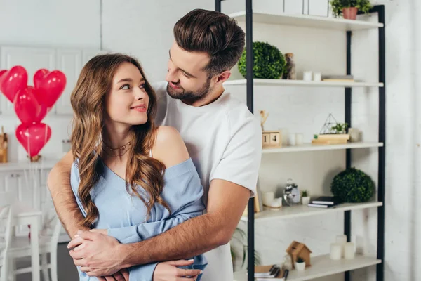 Selektiver Fokus des lächelnden Mädchens, das zärtlich seinen Freund anschaut, während der Mann Freundin im Zimmer mit Valentinstag-Dekoration umarmt — Stockfoto