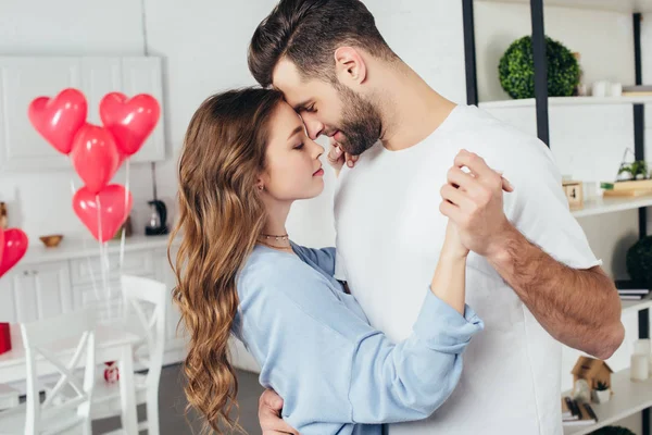 Enfoque selectivo de hermosa pareja feliz bailando en San Valentín con globos en forma de corazón en el fondo - foto de stock