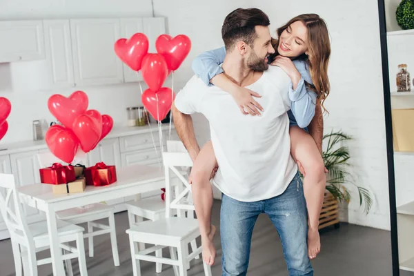 Heureux couple piggybackking à la maison dans la chambre avec st décoration Saint-Valentin — Photo de stock