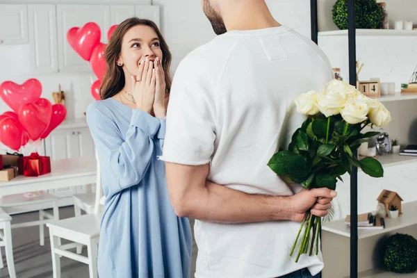 Teilbild eines jungen Mannes, der einen Rosenstrauß hinter sich hält, während seine lächelnde Freundin auf eine Überraschung wartet — Stockfoto
