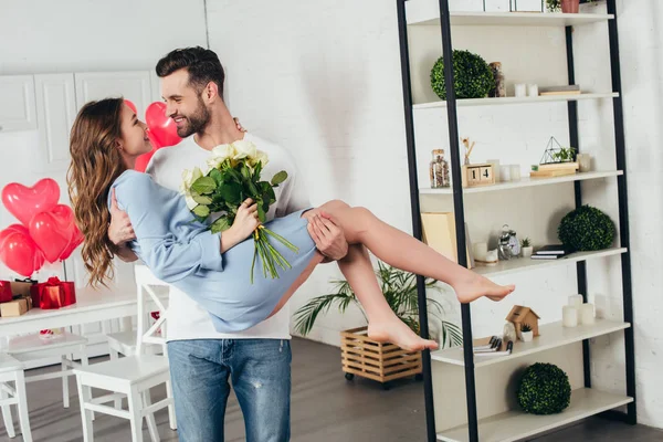 Feliz casal celebrando st dia dos namorados, enquanto jovem segurando sorridente namorada com rosas buquê nos braços — Fotografia de Stock