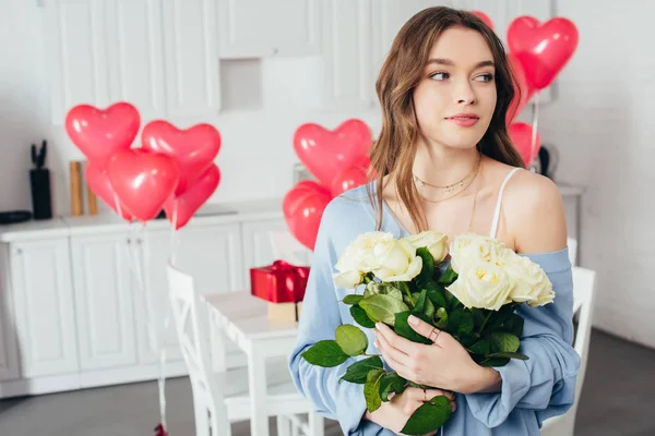 Enfoque selectivo de una chica sonriente sosteniendo ramo de rosas en la habitación decorada con globos en forma de corazón - foto de stock