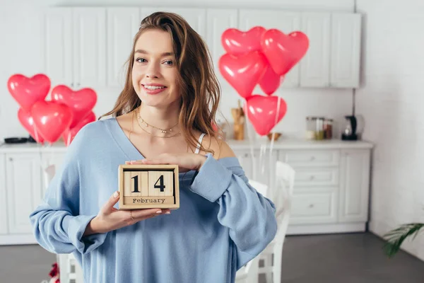 Menina sorridente feliz segurando calendário de madeira com data do dia de São Valentim em casa — Fotografia de Stock