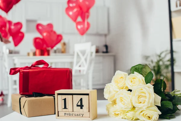 Geschenkboxen mit Schleifen, Rosenstrauß und Kalender mit Valentinstag Datum auf dem Tisch mit herzförmigen Luftballons auf dem Hintergrund — Stockfoto