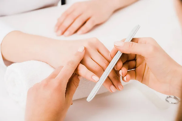 Cropped view of manicurist gently filing natural nails for customer — Stock Photo