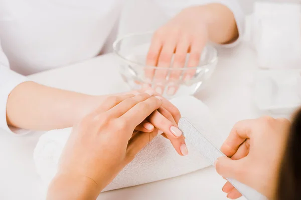 Partial view of manicurist holding female hand and using nail file — Stock Photo