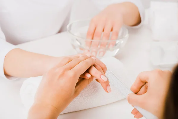 Vista parcial de la manicura sosteniendo la mano femenina y usando una lima de uñas - foto de stock