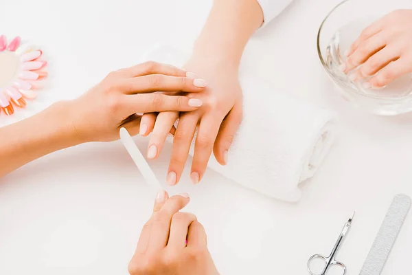 Vista parcial da mulher fazendo banho de mão enquanto manicure usando o arquivo de unhas — Fotografia de Stock