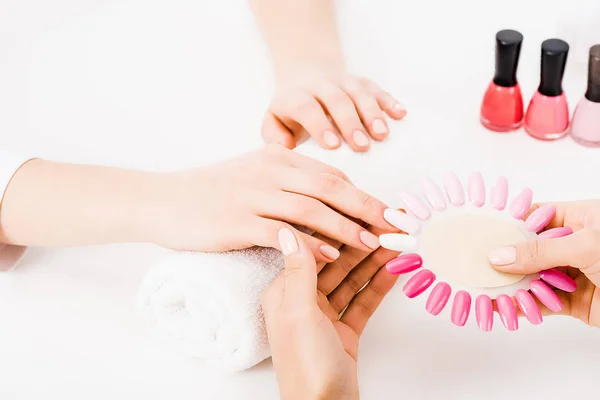 Vista ritagliata della manicure tenendo tavolozza smalto mentre si sceglie il colore — Foto stock